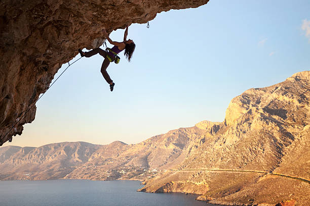 силуэт молодой женский рок альпинист на утесе - rock climbing стоковые фото и изображения