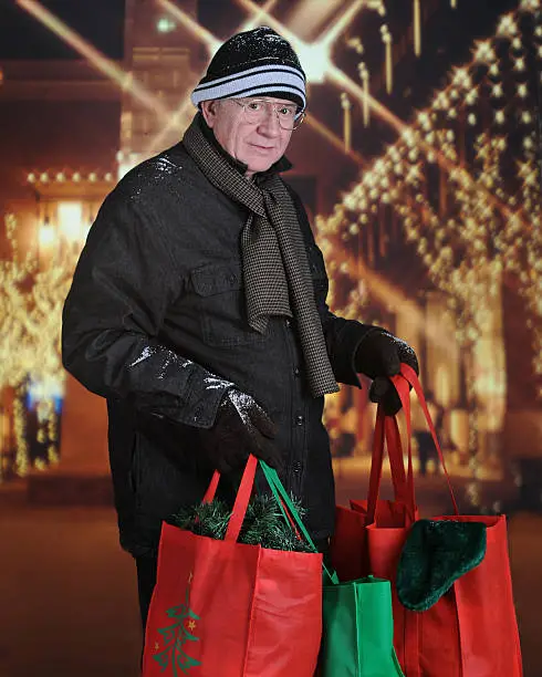 A senior man happily carrying filled shopping bags outside from a Christmas decorated mall.
