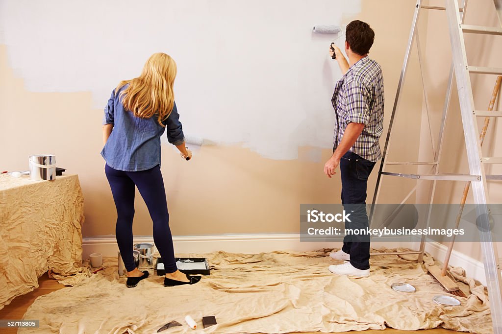 Couple Decorating Room Using Paint Rollers On Wall 30-39 Years Stock Photo