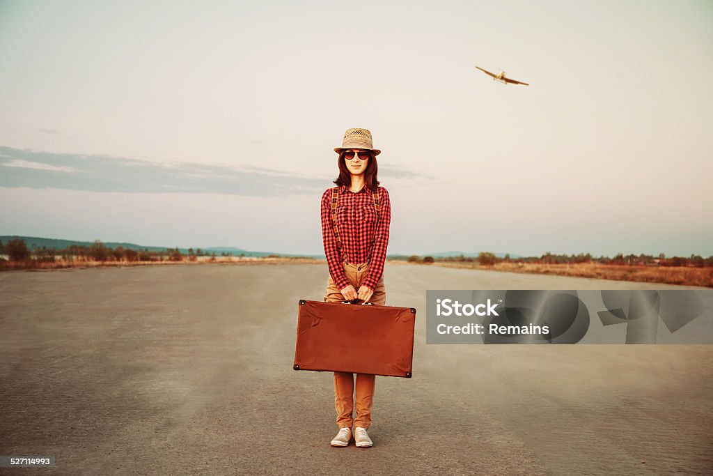Traveler standing with suitcase on road Traveler woman standing on road with vintage suitcase, airplane in sky. Space for text Adult Stock Photo