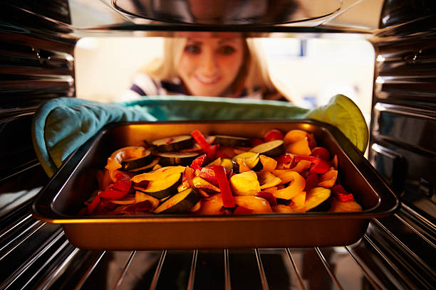 mujer poniendo platos de vegetales en horno a la parrilla - roasted vegetable fotografías e imágenes de stock