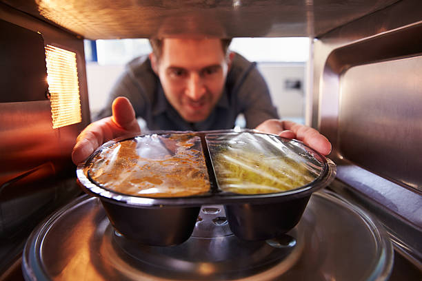 Man Putting TV Dinner Into Microwave Oven To Cook Man Putting TV Dinner Into Microwave Oven To Cook inside microwave stock pictures, royalty-free photos & images
