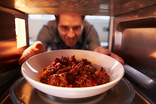 Man Putting Leftover Chili Into Microwave Oven To Cook Man Putting Leftover Chili Into Microwave Oven To Cook, Smiling inside microwave stock pictures, royalty-free photos & images
