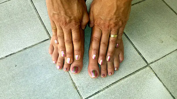 Toes and fingers with bi-color nailpolish on tile floor