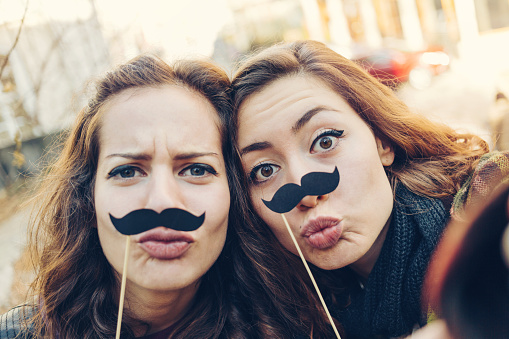 Girls making face expressions selfie with fake mustaches