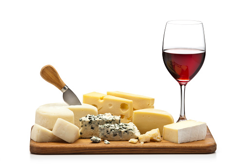 Front view of a wooden platter filled with a variety of cheeses and a red wine glass isolated on white background. DSRL studio photo taken with Canon EOS 5D Mk II and Canon EF 100mm f/2.8L Macro IS USM