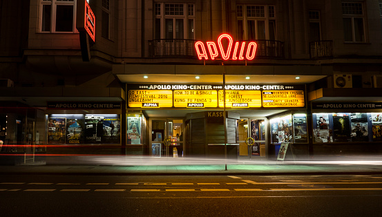 Wiesbaden, Germany - April 26, 2016: Entrance, facade and neon sign of Apollo cinema center in the city center of Wiesbaden. Apollo is a well-known, long-established cinema center consisting of five cinema halls. Some motion blurred headlights in front of the building