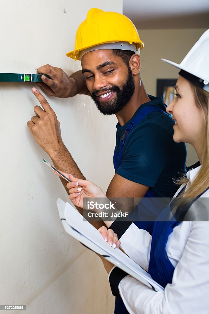 Engineers at the work Smiling blonde female engineer checking black specialist making wall plane  . Focus on man Adult Stock Photo