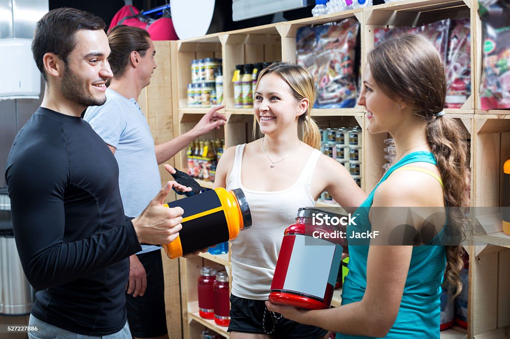 Group of young adults discussing bodybuilding supplements Happy group of young adults discussing bodybuilding supplements in gym. Focus on the blonde woman Acid Stock Photo