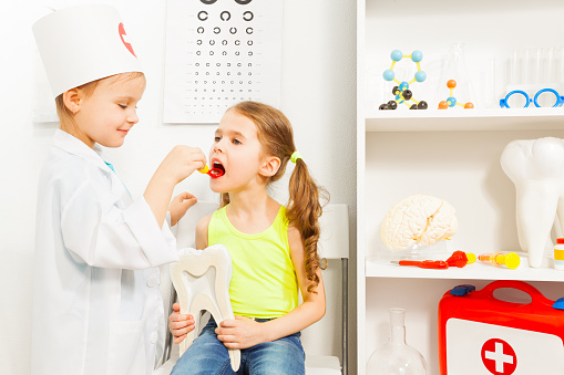 Little girl playing a dentist with her friend at the medical room
