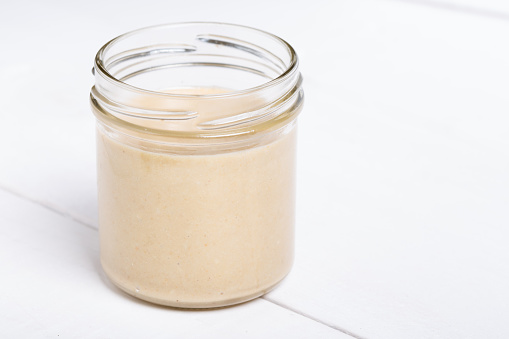 Homemade DIY natural vegan very healthy tahini paste made of sesame seeds in a glass jar on a wooden table