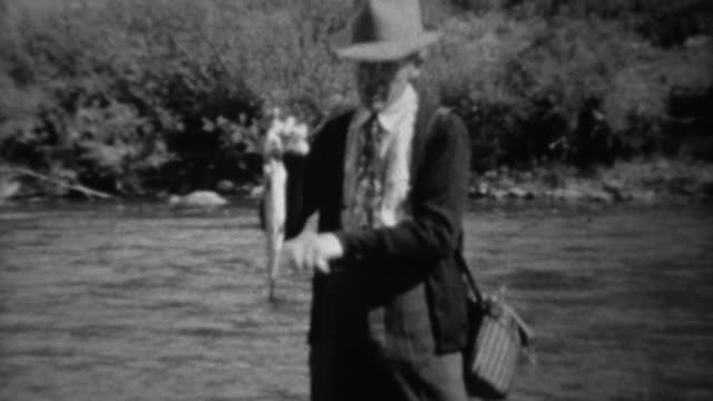 1939: Fisherman wading in fast stream showing trout fish catch.