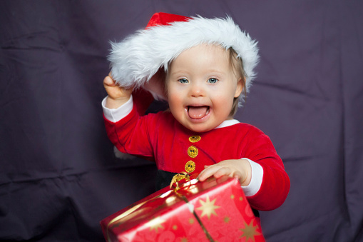 Christmas baby with a wrapped gift and funny Santa Clause outfit. Merry and cheerful. Cute Sweetheart!