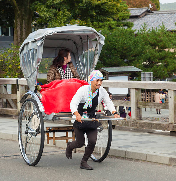 Kyoto, Japan - November 3, 2014: A tourist riding a rickshaw in Arashiyama, a tourist district in Kyoto, Japan. Rickshaw is a popular mode of transportation in Japan in the 19th century. Rickshaw's popularity has declined by the 1930s but they can still be found in some tourist areas in Kyoto and Tokyo.The rickshaw runners also work as tourist guides, who take their clients to tourist spots.