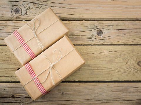 two brown paper parcels with red check ribbon against an aged wooden background