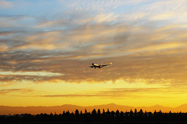 Jumbo Jet Airplane landing near Los Angeles California with a beautiful colorful sunrise and mountain silhouette in the background