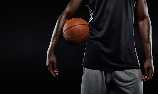 Cropped image of afro american basketball player holding a ball against dark background