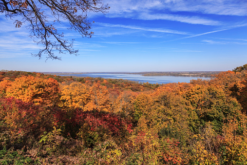 A scenic view of the Illinois River from high atop the bluffs on Grandview Drive in Peoria, Illinois. The fall colors of the trees are glowing set against the blue sky and the river in the distance. The Illinois River around Peoria, Illinois was the home of many Indian tribes because of the great access to water and abundant wildlife for hunting and fishing.