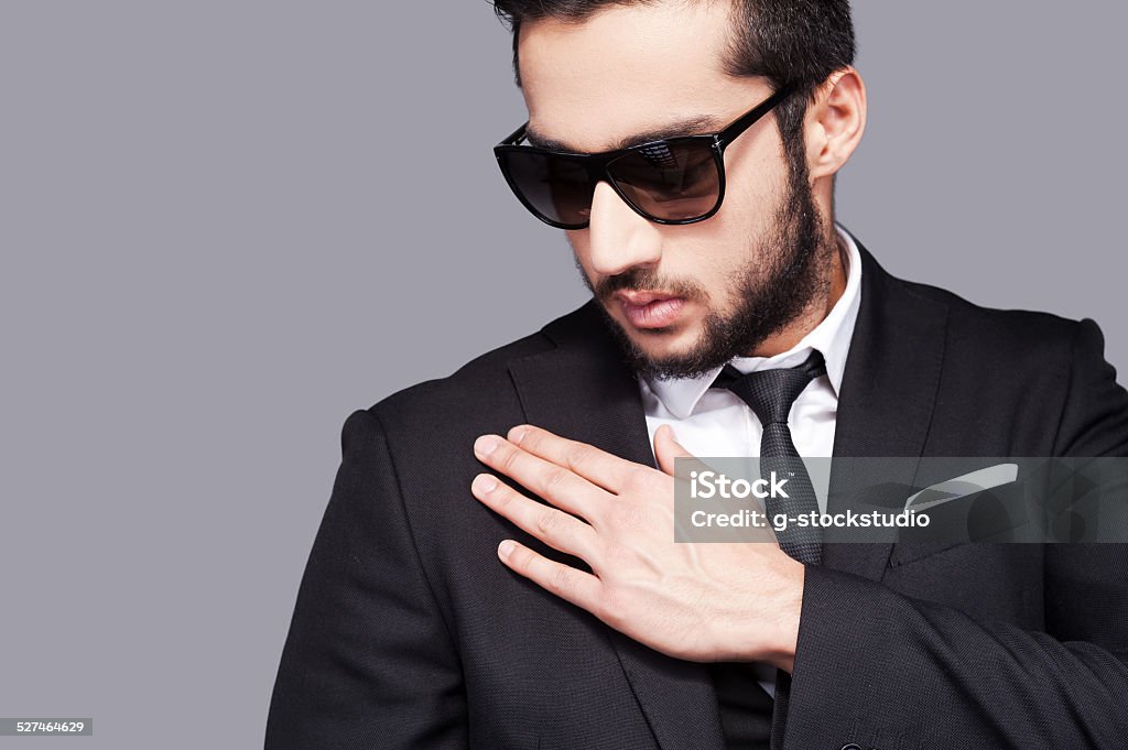 Used to look perfect. Handsome young man in sunglasses and formalwear touching his shoulder with hand while standing against grey background Adult Stock Photo