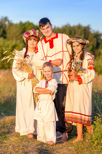 Beautiful family in Russian folk costumes standing together outdoors at summer sunset