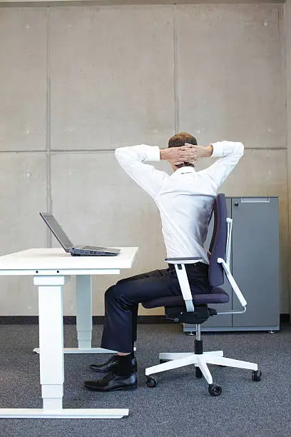 exercises in office. business  man with arms on head  sitting on office armchair at the desk - back view