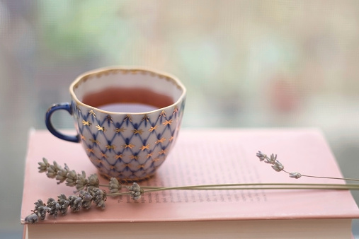 Tea in a vintage porcelain cup, with lavender and old book. Shallow depth of field and soft focus.