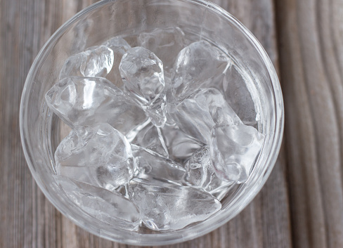 horizontal image of a clear glass bowl of ice cubes melting on a wooden background.