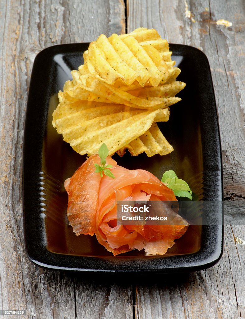 Smoked Salmon and Potato Chips Delicious Smoked Salmon with Rifled Potato Chips on Black Plate isolated on Rustic Wooden background Appetizer Stock Photo