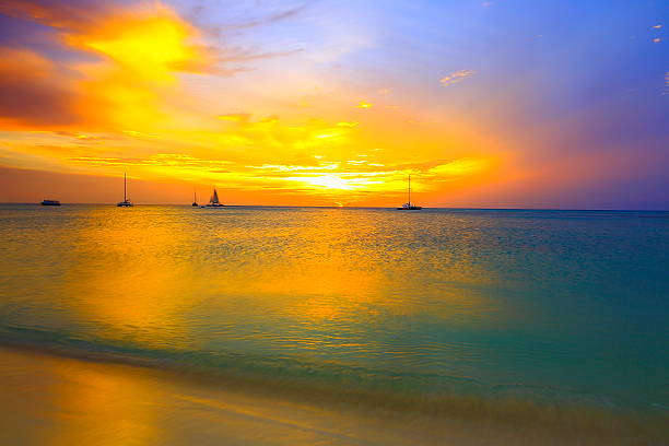 idillio drammatico tramonto e navi in palm beach, aruba, caraibi - sailing sailboat sunset aruba foto e immagini stock