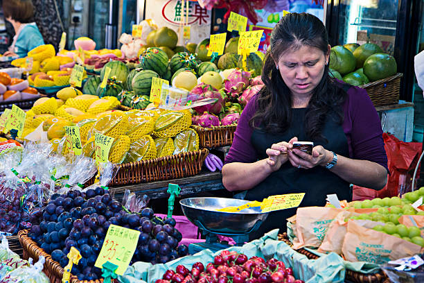 Hong Kong, Сhina - November 9, 2014: Asian woman at her fruit market stand checking the mobile phone.