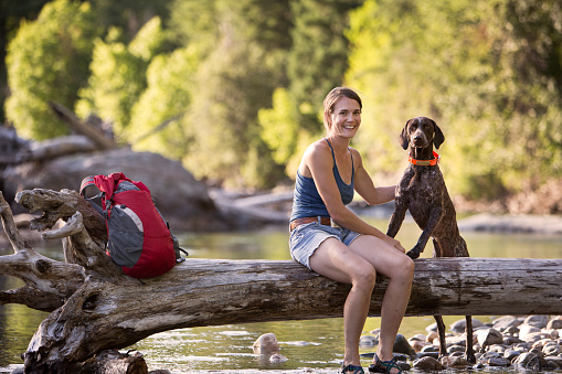A hiker and her dog sitting by a mountain stream.