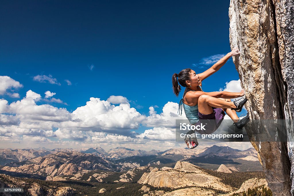 Rock climber clinging to a cliff. Female climber dangles from the edge of a challenging cliff. Rock Climbing Stock Photo