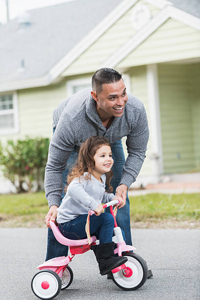 istock Hispanic father helping daughter ride tricycle 527533550