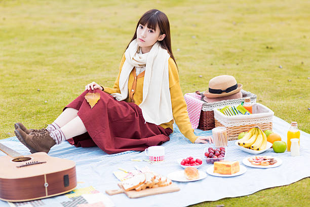 sat a beautiful park in the lawn chinese girl, there are a lot of food, bread, fruit, drinks on the lawn