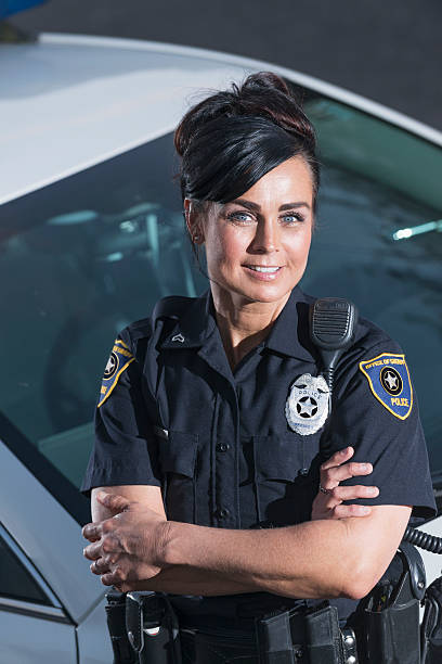 Policewoman standing next to police car, arms crossed A female police office standing next to her patrol car with her arms crossed, looking at the camera with a happy, confident expression. female police officer stock pictures, royalty-free photos & images