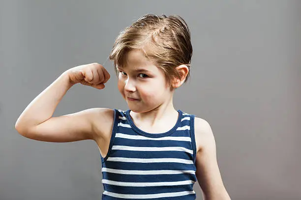 Little Sportive Tough Boy in striped  muscle shirt, showing his muscles, smiling in Camera