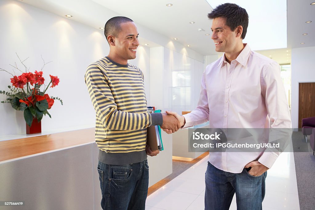 Multiethnic Businessmen Shaking Hands In Office Casually dressed happy multiethnic businessmen shaking hands in office Adult Stock Photo