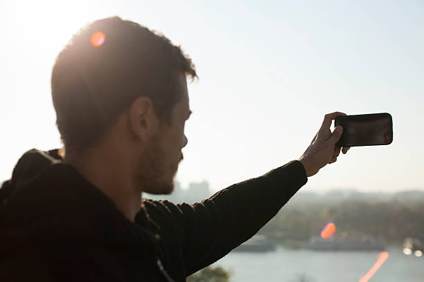 Hombre tomando fotos de la ciudad y al río con teléfono móvil - foto de stock