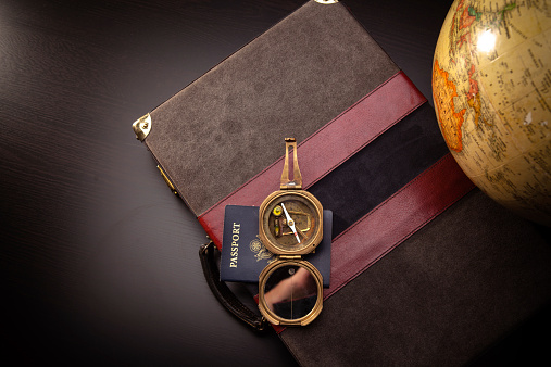 Evocative still life shot of an old fashioned brass compass, a sepia toned globe with a briefcase and a modern US passport.