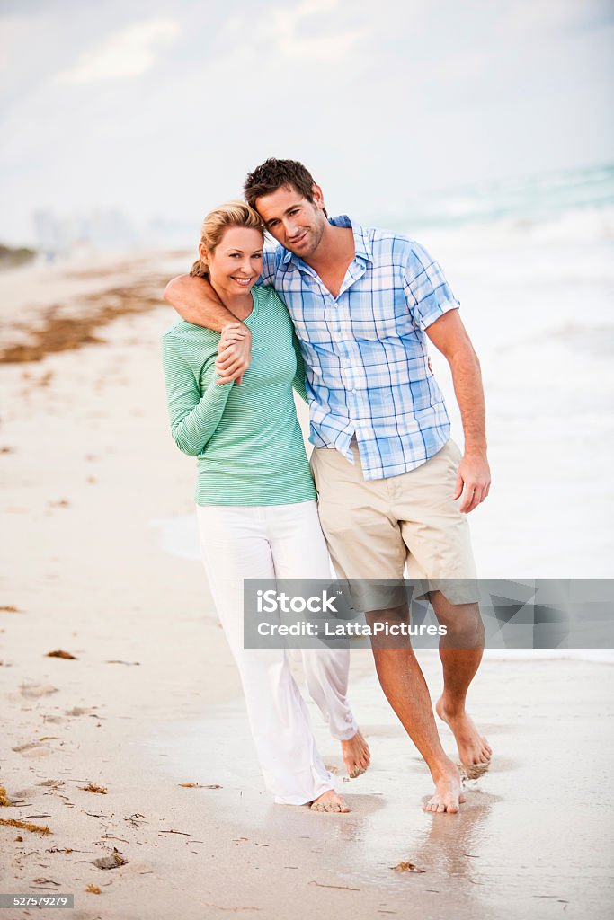 Loving couple walking on beach embracing Mid adult couple embracing and strolling on water's edge 30-39 Years Stock Photo