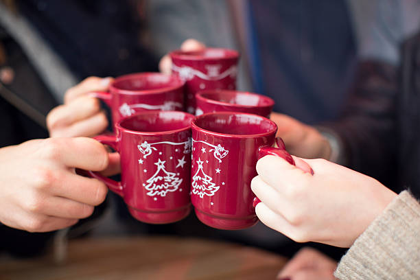 Friends having hot drinks outdoors in winter city. Close up of hands holding cups with hot wine at outdoor cafe on a street, christmas market. Cups are decorated with christmas tree ornament. Vienna, Austria. mulled wine stock pictures, royalty-free photos & images