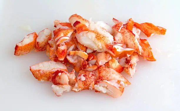 Chunks of cooked cut lobster meat on a plastic white cutting board.
