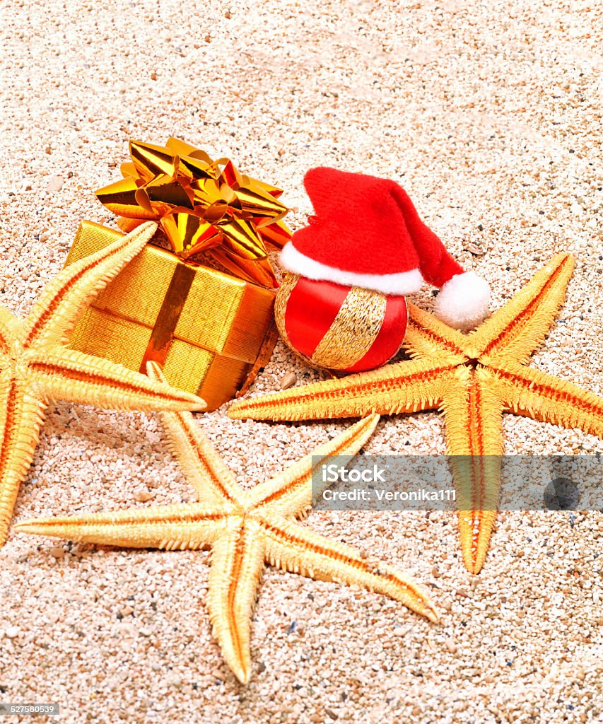 christmas ball, starfishes and a gift box on  sand christmas hat, starfishes, christmas bauble and a gift box on the sand Beach Stock Photo