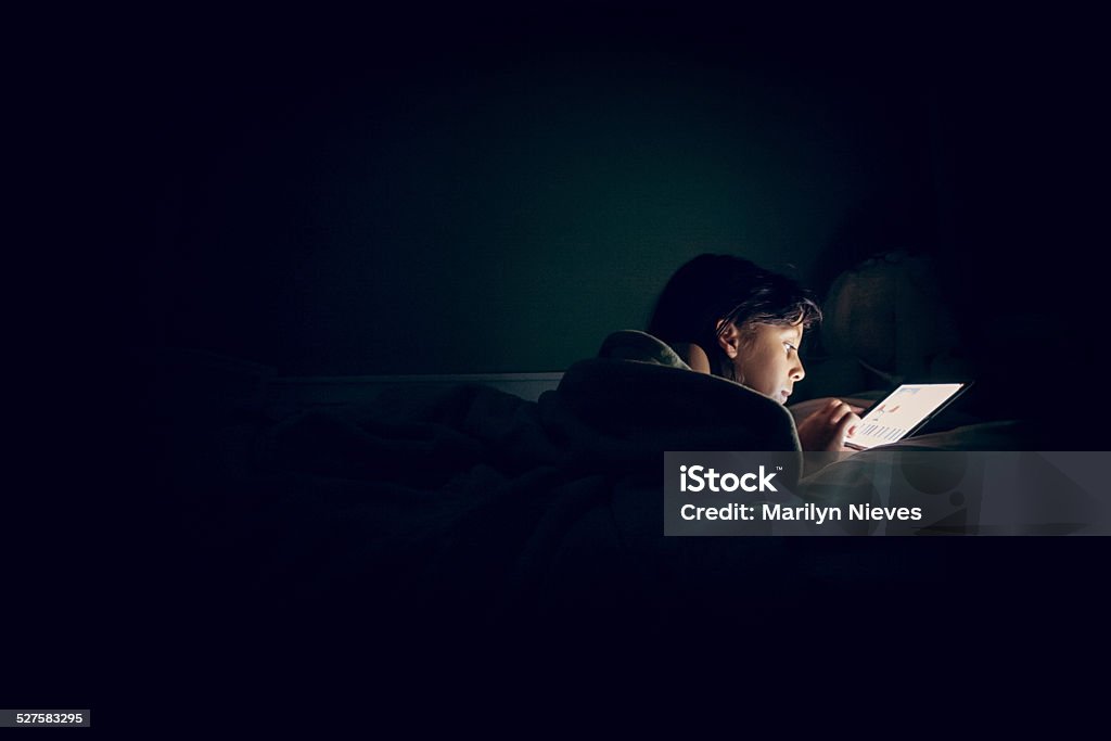 child reading tablet in bed at night Young girl reading her digital tablet on her bed at night with an intrigued look. Child Stock Photo