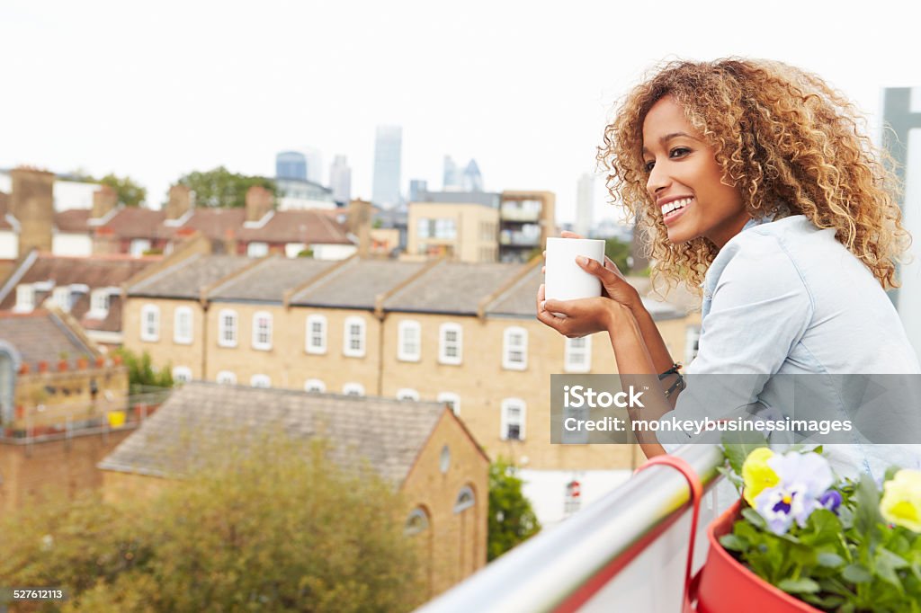 Woman Relaxing Outdoors On Rooftop Garden Woman Relaxing Outdoors On Rooftop Garden, Holding Mug, Smiling Off Camera Balcony Stock Photo