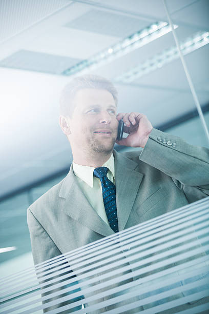 Businessman on the phone in office. View through the glass wall with white stripes.