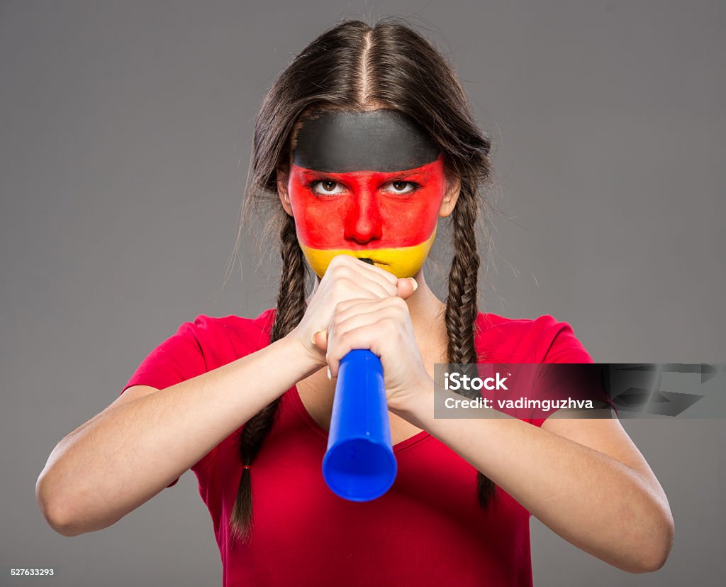Face art. Flags. Flag of Germany painted on a face of a young woman with vuvuzela.Flag of Germany painted on a face of a young woman.Flag of Germany painted on a face of a young woman.Flag of Germany painted on a face of a young woman. She is holding the soccer ball. Adult Stock Photo