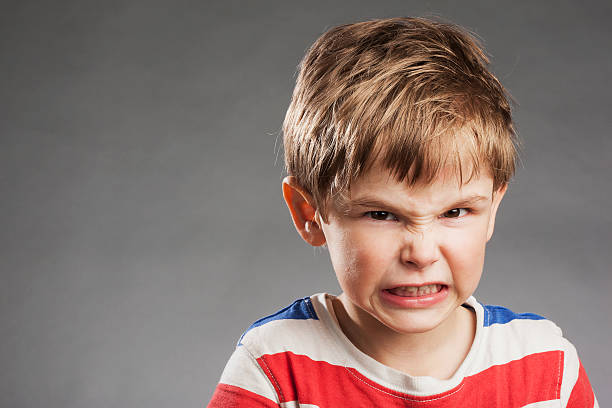 istock Young boy looking angry, clenching teeth against gray background 527634489