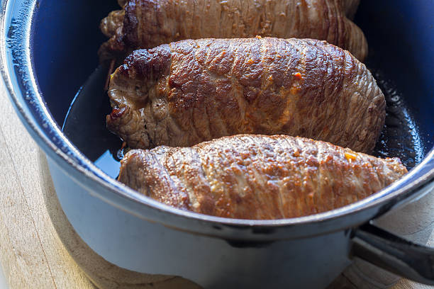 Roulade of beef in pan with sauce.