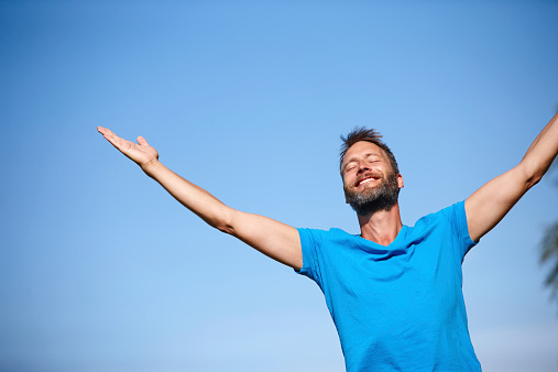 Cropped shot of a carefree mature man standing with his arms outstretched against a blue sky